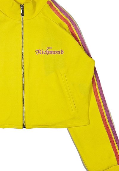 Giacca gialla corta con zip, realizzata in un tessuto morbido, con strisce rosa e viola lungo le maniche e la scritta "John Richmond" stampata sul davanti.