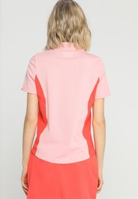 Kortärmad polotröja med en rosa front och korallfärgade sidopaneler. Tillverkad av ett texturerat tyg med rundad nederkant och krage.