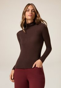 Top marrone a maniche lunghe con collo alto, dal design aderente e texture liscia, abbinato a pantaloni color bordeaux.