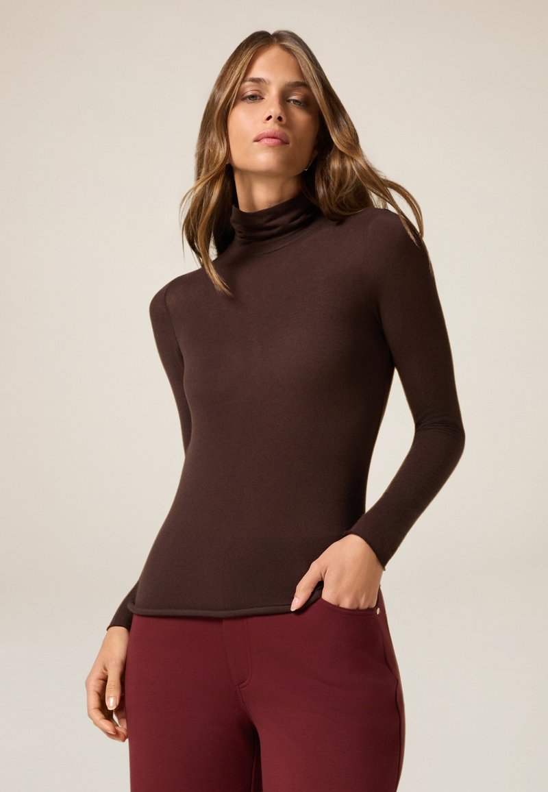 Top marrone a maniche lunghe con collo alto, dal design aderente e texture liscia, abbinato a pantaloni color bordeaux.