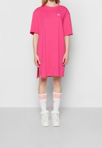 Rosa oversized t-shirt klänning med korta ärmar och sidofickor. Kombinerad med vita strumpor med rosa ränder och vita sneakers.