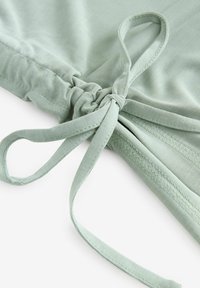 Tissu en coton vert menthe avec un détail de nœud et une fermeture à nouer. Texture lisse avec un léger stretch et des finitions cousues le long des bords.