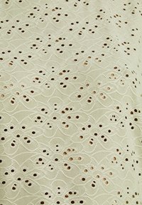 Tissu beige avec des motifs floraux brodés et des œillets créant un motif de dentelle délicat et texturé.