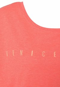 Camiseta de color coral con escote redondeado, que presenta un gráfico de texto en beige claro que dice "VENECIA". Textura de tela suave y lisa.
