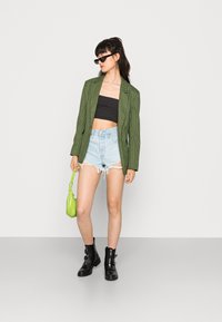 Blazer xadrez verde, top cropped preto, calções rasgados azul claro, botins pretos e pequena mala verde.