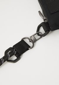 Czarny pasek torby z tkaniny o teksturowanej powierzchni, z metalowymi akcesoriami w matowym wykończeniu i plecionym wzorem z białymi akcentami.
