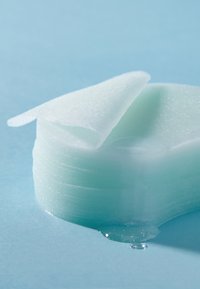 En stak af gennemsigtige, lyseblå geléagtige plader med en glat overflade, let buet på toppen, som ligger på en blå overflade med dråber.