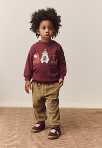 Sweat-shirt bordeaux avec broderie d'animal, pantalon beige à côtes et baskets bordeaux. Encolure arrondie, coupe décontractée et poches latérales.
