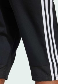 Pantalones cortos atléticos negros con diseño de triple raya blanca en los lados, con una textura suave y un corte hasta la rodilla.