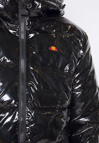 Černá lesklá prošívaná bunda s uzavřením na zip, horizontálním prošíváním a vyšívaným logem v oranžové a žluté barvě.