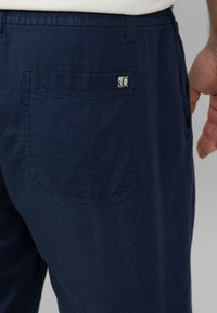 Pantalons bleu marine en tissu léger ; dotés d'une poche arrière avec une étiquette logo et d'une coupe décontractée.