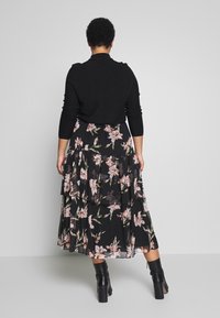 Maglione aderente nero con maniche lunghe abbinato a una gonna maxi a volant con un motivo floreale in rosa e verde su uno sfondo nero.