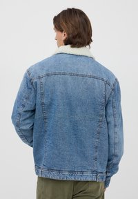 Giacca di jeans blu chiaro con colletto in shearling, vestibilità rilassata e dettagli cuciti lungo le cuciture. La vista posteriore non mostra tasche.