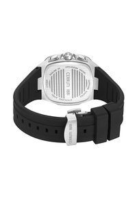 Siverfärgad rostfri stålklocka med en texturerad baksida, vattentålig, och en svart silikonslunga som är fäst med en silverfärgad spänne.