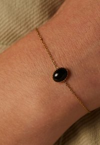 Gold chain bracelet with an oval black stone centerpiece. Chain features small links and intricate detailing around the stone.