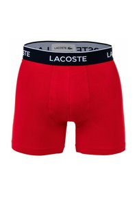 Piros pamut boxer nadrág, fekete elasztikus derékpánttal, rajta fehér "Lacoste" logóval és testhez simuló szabással.