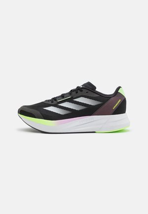Le scarpe da atletica nere presentano una tomaia in mesh con dettagli riflettenti e tre strisce bianche. La suola include rifiniture verdi e rosa.