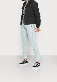 Černá zkrácená bunda s kapucí, nosící se přes vzorovanou košili, spárovaná se světle modrými džíny s vysokým pasem a černými teniskami.