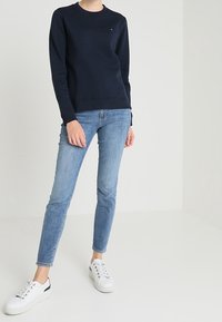 Felpa in cotone blu navy con colletto rotondo, abbinata a jeans skinny azzurri chiari e sneakers bianche con occhielli in argento e dettagli neri.