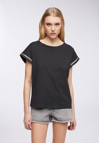 T-shirt in cotone nero con maniche corte arrotolate, caratterizzato da cuciture metalliche a contrasto. Design semplice, vestibilità morbida e rilassata, texture soffice.