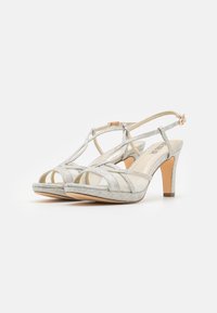 Silver strappy heels featuring a textured woven pattern, open toe design, and a mid-height heel with an adjustable ankle strap.