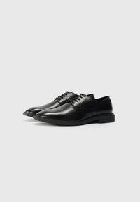 Zwarte leren dresschoenen met een gladde afwerking, ronde neus, vetersluiting en platte rubberen zolen. Voorkeur voor subtiele stikdetails op het bovendeel.