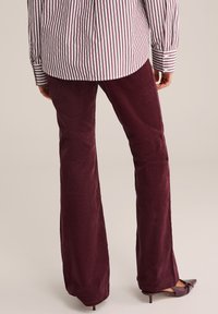 Burgundy kordbársonyos harangnadrág, puha textúrával, magas derékkal, csíkos, gombos inggel és hegyes orrú magassarkú cipővel párosítva.