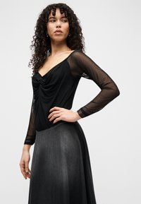 Μαύρο τοπ με μακριά μανίκια, με draped μπροστινή όψη και διάφανα μανίκια, συνδυασμένο με μια ρέουσα σκουρόγρια φούστα με ομαλή υφή.