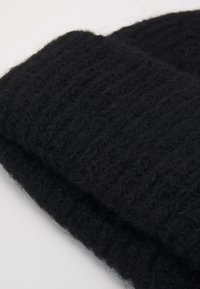 Fekete kötött sapka texturált mintával, puha fonalból készült, vastag bordázott szegéllyel és kényelmes megjelenéssel.
