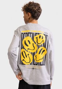 Langärmliges graues T-Shirt mit großen gelben Smileys und auffälligem schwarzen Text auf der Rückseite. Aus weichem Baumwollmaterial, entspannte Passform.