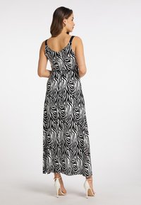 Maxime Kleid im schwarz-weißen Zebra-Muster, mit einer taillierten Taille, breiten Trägern und einem fließenden Stoff. Geschlossene Absatzschuhe setzen einen Kontrast.