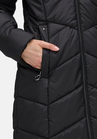 Czarna kurtka puchowa z haftem w zygzak, zamkiem z przodu oraz bocznymi kieszeniami z dyskretnym okuciem i teksturowanym wykończeniem.