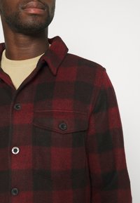 Rood-zwart geruit flanellen overhemd met kraag, één borstzak en zwarte knopen, met een zachte textuur en een gestructureerd ontwerp.