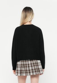 Maglione corto black in maglia con maniche lunghe, abbinato a una gonna plissettata a quadratini con tonalità bianche, marroni e nere.
