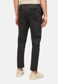 Sorte bukser med tern, tætsiddende pasform, elastisk talje og to baglommer. Stoffet har en glat tekstur og et subtilt ternet mønster.