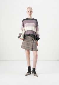 Knitted sweater with purple, white, and dark green stripes, paired with a plaid brown skirt featuring a belt. Holding a beige handbag.