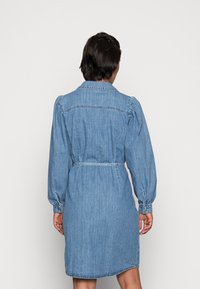 Denimklänning, ljusblå, med långa puffärmar, krage, åtstramad midja och bakfickor. Slät textur och rak nederkant.