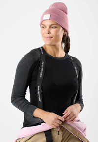 Maglia nera a maniche lunghe con maniche grigie, caratterizzata da una tracolla con il logo Swedemount visibile. Un berretto a maglia rosa si abbina a pantaloni beige con un accento rosa.
