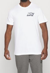 Camiseta de algodón blanca con un logo gris de "NIKE" en el pecho. Manga corta, cuello redondo y un diseño de ajuste estándar.