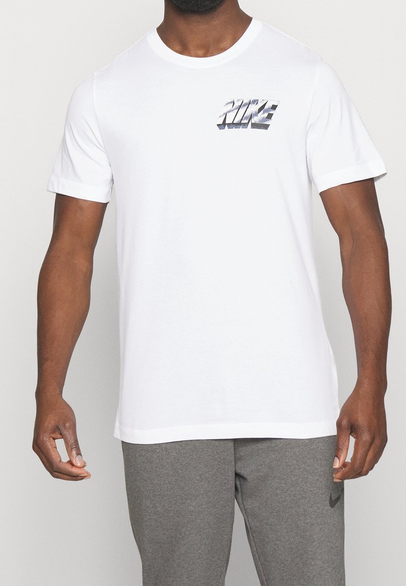Camiseta de algodón blanca con un logo gris de "NIKE" en el pecho. Manga corta, cuello redondo y un diseño de ajuste estándar.