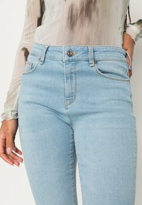 Jeans de cintura alta azul claro com um design ajustado, apresentando um fecho de botão de metal, bolsos frontais e uma textura de denim suave.