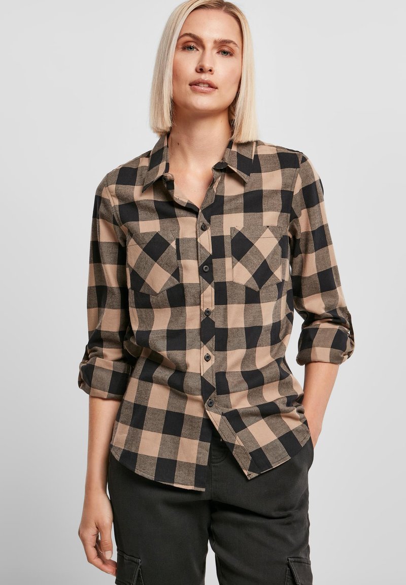 Chemise à carreaux noir et beige avec un devant à boutons, deux poches sur la poitrine et des manches retroussées, fabriquée en tissu doux avec une texture lisse.