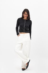 Zwarte lange mouwen crop top met witte rand en knopen, gecombineerd met losse witte broeken en zwarte ballerina's.