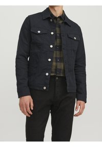 Mörkblå denimjacka med silverknappar, två bröstfickor och en spetsig krage. Bärs över en rutigt skjorta i grönt och svart.