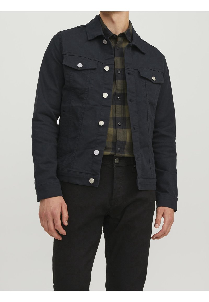 Mörkblå denimjacka med silverknappar, två bröstfickor och en spetsig krage. Bärs över en rutigt skjorta i grönt och svart.