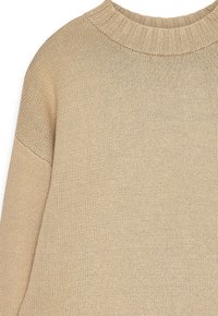 Beige stickad tröja med ribbad rundhalsning och långa ärmar, som visar en detaljerad struktur av stickat tyg.