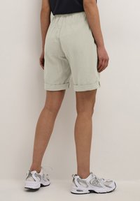 Pantalones cortos de corte relajado en verde claro con dobladillos enrollados, cintura elástica y tejido texturizado. Llevados con zapatillas deportivas blancas y plateadas.