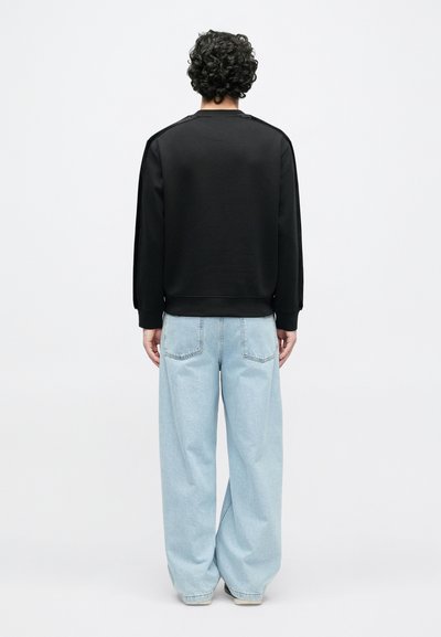 Melna sporta džemperis ar apaļu kakla izgriezumu un garām piedurknēm, kombinēts ar gaiši zilām plaša piegriezuma džinsu biksēm ar aizmugurējām kabatām. Gluda auduma tekstūra.
