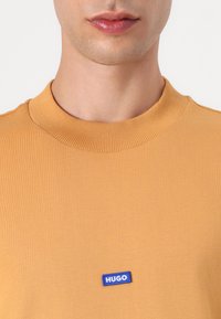 Khaki crew neck t-shirt lavet af ribbet stof, med et lille blåt "HUGO" mærke foran. Glat tekstur med en tætsiddende form.