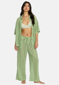 Set in maglia a uncinetto verde chiaro composto da una camicia oversize a maniche corte con bottoni, pantaloni ampi abbinati e un reggiseno a fantasia floreale.